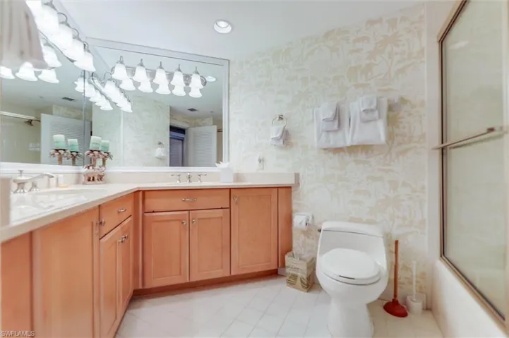 Bathroom featuring double vanity, wallpapered walls, bath / shower combo with glass door, light tile patterned flooring, and recessed lighting