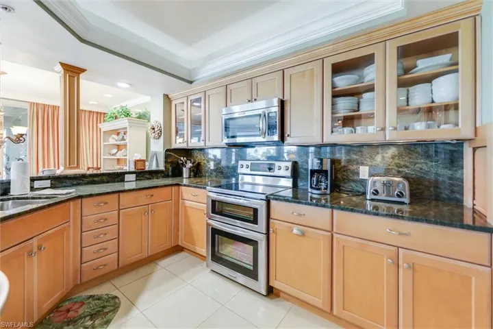 Kitchen featuring glass insert cabinets, stainless steel appliances, dark stone counters, crown molding, and tasteful backsplash
