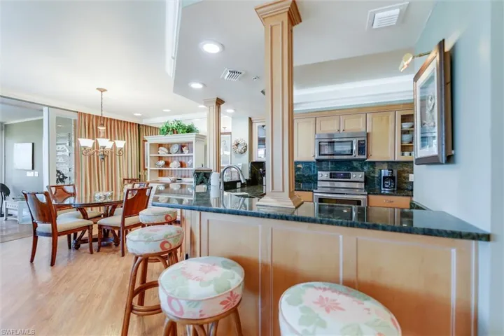 Kitchen with decorative columns, stainless steel appliances, dark stone countertops, a chandelier, and a peninsula
