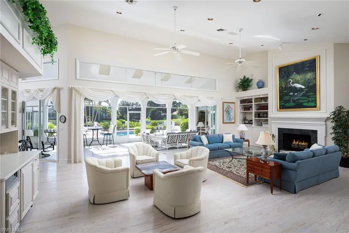 Living room featuring high vaulted ceiling, a lit fireplace, light wood-style flooring, built in features, and recessed lighting