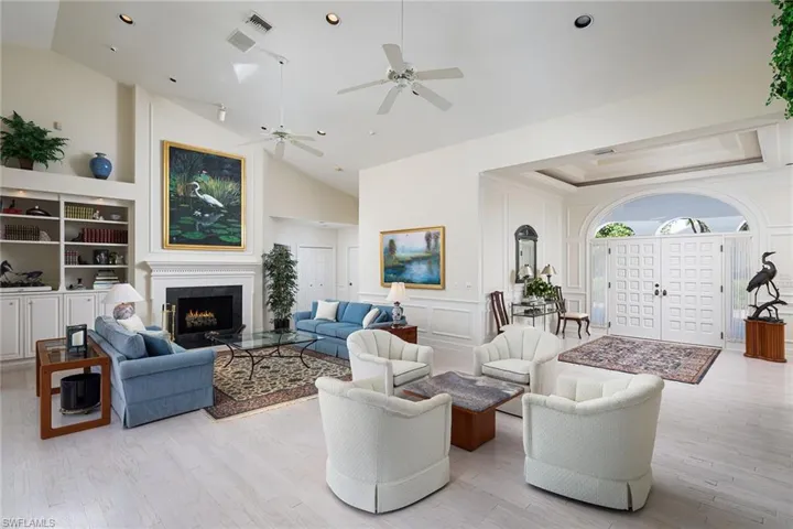 Living area with a warm lit fireplace, light wood finished floors, a decorative wall, high vaulted ceiling, and a ceiling fan