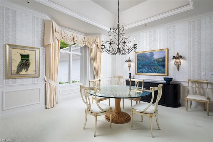 Carpeted dining space with wallpapered walls, a decorative wall, a wainscoted wall, crown molding, and a chandelier