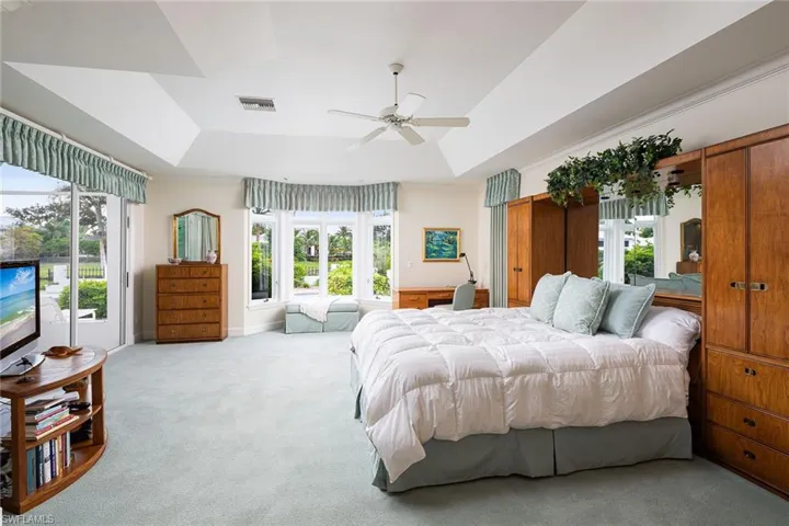 Carpeted bedroom featuring ceiling fan, multiple windows, a tray ceiling, and access to outside