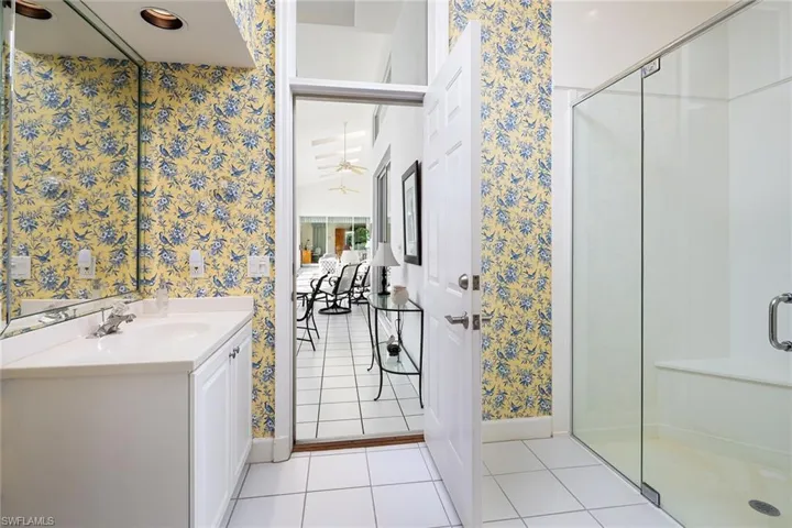 Full bath featuring light tile patterned floors, vanity, wallpapered walls, and a stall shower
