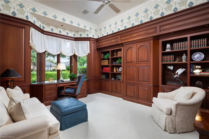 Carpeted home office featuring built in study area, wallpapered walls, crown molding, and a ceiling fan