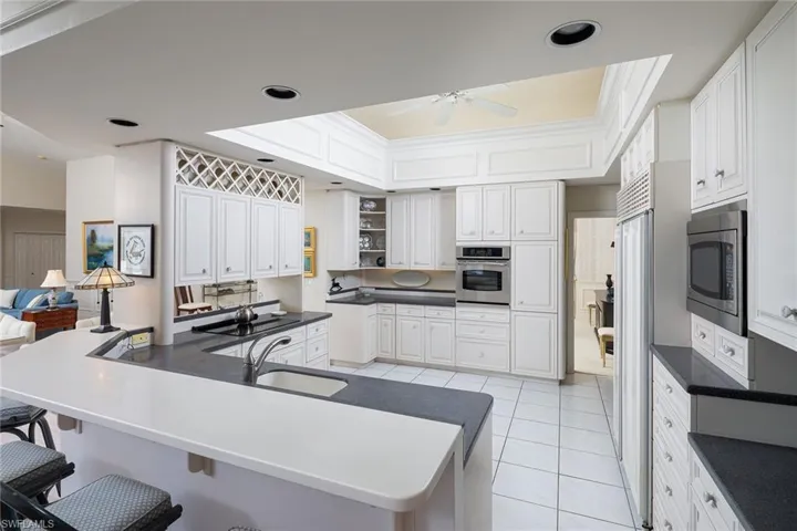 Kitchen with white cabinets, dark countertops, light tile patterned floors, a peninsula, and crown molding