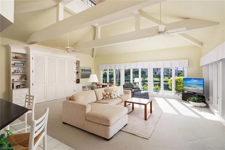 Living area featuring a ceiling fan, high vaulted ceiling, light colored carpet, and beam ceiling