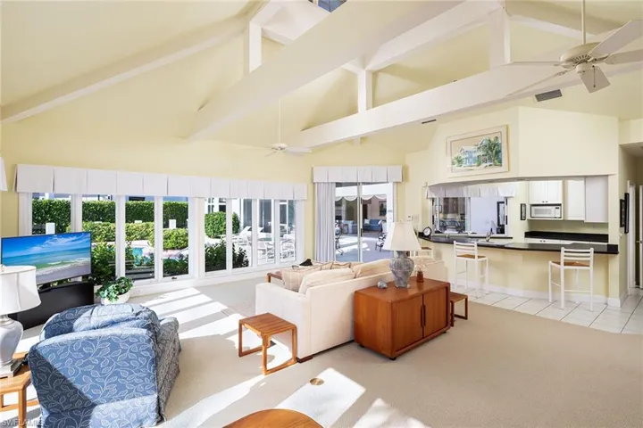 Living room with ceiling fan, high vaulted ceiling, light colored carpet, and beamed ceiling