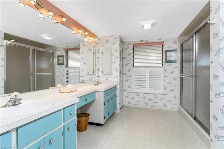 Bathroom with wallpapered walls, light floors, a stall shower, and double vanity