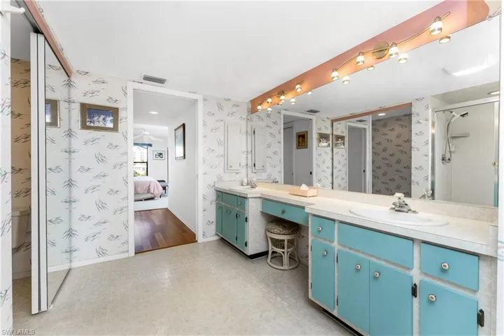 Full bathroom with double vanity, wallpapered walls, connected bathroom, light floors, and a shower stall