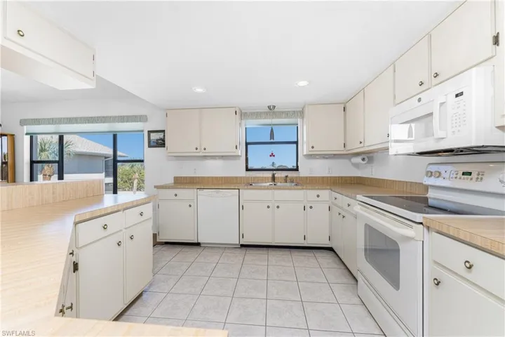 Kitchen with white appliances, light countertops, recessed lighting, and white cabinets