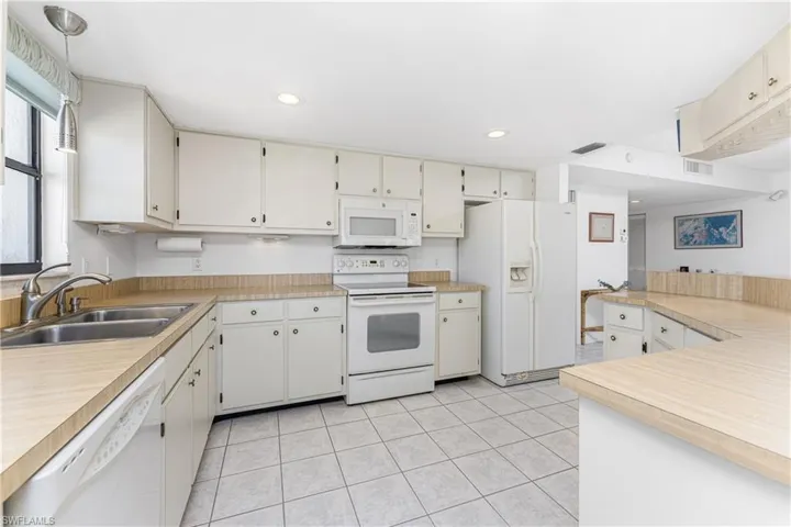 Kitchen with white appliances, light countertops, light tile patterned flooring, white cabinets, and decorative light fixtures