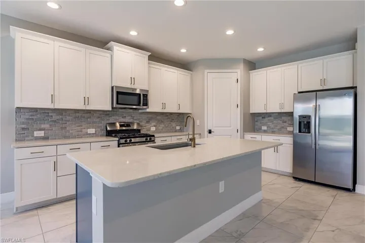 Kitchen featuring white cabinets, backsplash, appliances with stainless steel finishes, and sink