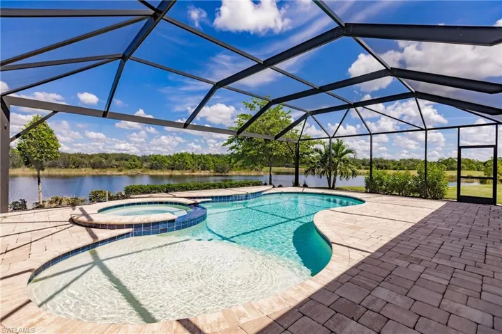 View of pool with a lanai, a patio, a water view, and an in ground hot tub