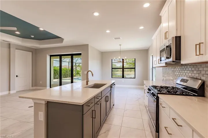 Bright kitchen with white shaker cabinets, stainless steel appliances, gas range/oven, counter height island and brass cabinet pulls and faucet.