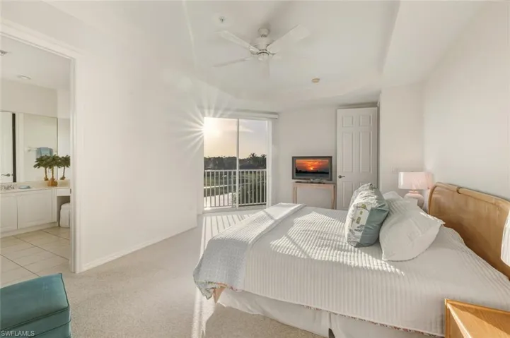 Bedroom featuring light colored carpet, access to outside, ceiling fan, ensuite bath, and a tray ceiling