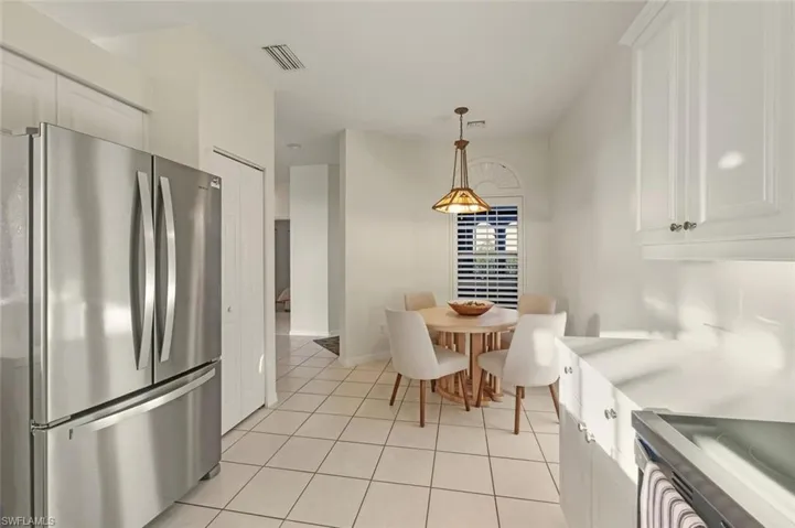 Kitchen featuring freestanding refrigerator, white cabinetry, decorative light fixtures, electric range, and light tile patterned floors