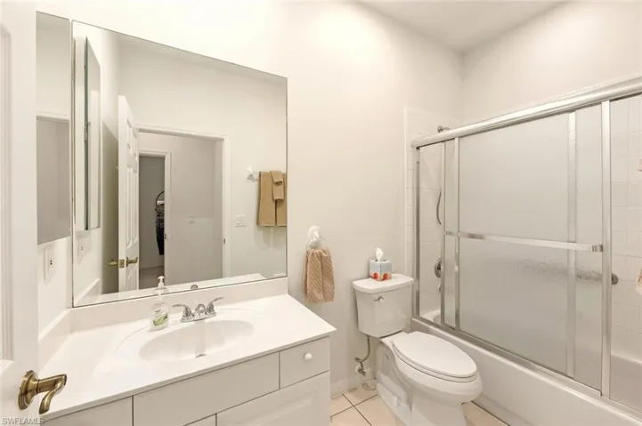 Full bath featuring combined bath / shower with glass door, vanity, and light tile patterned floors