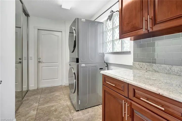 Laundry room featuring solid wood cabinet  and stacked washer / dryer, and light tile patterned flooring.