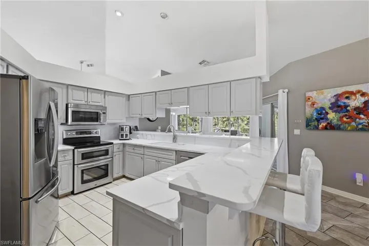 Kitchen with stainless steel appliances, lofted ceiling, a peninsula, a kitchen breakfast bar, and light gray cabinetry