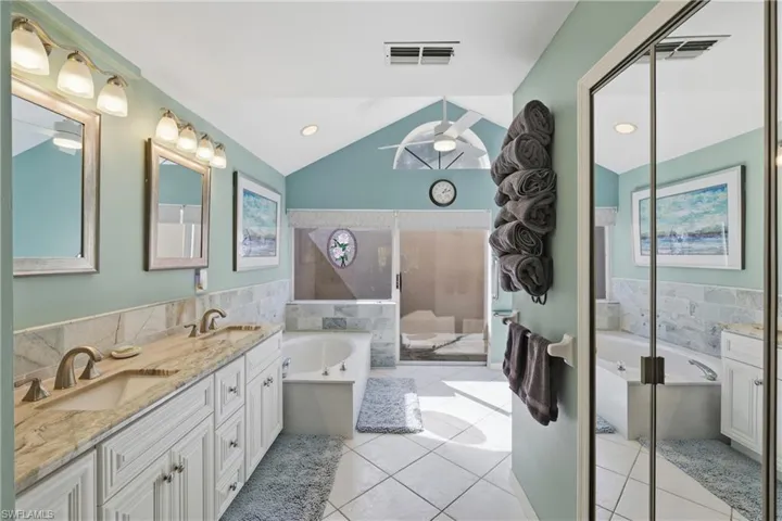 Full bath featuring a bath tub, double vanity, vaulted ceiling, light tile floors, and a tiled shower