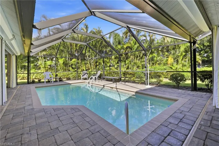 Swimming pool featuring a patio area, screen enclosure, and a lush backyard