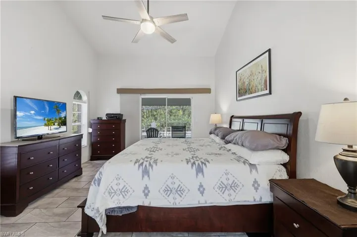 Primary Bedroom featuring sliding glass doors to the screened pool lanai, a ceiling fan, and high vaulted ceiling