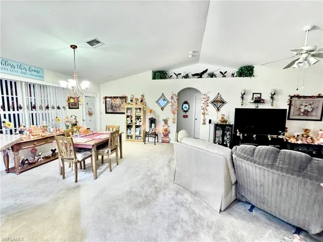 Living area with vaulted ceiling, light colored carpet, arched walkways, ceiling fan, and a chandelier