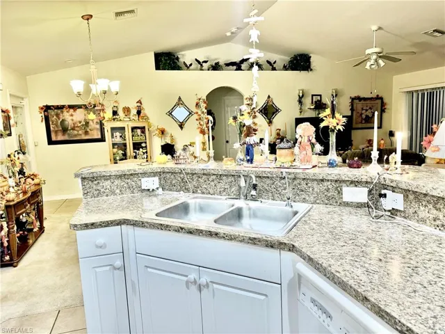 Kitchen with light tile patterned flooring, light colored carpet, dishwasher, vaulted ceiling, and a chandelier