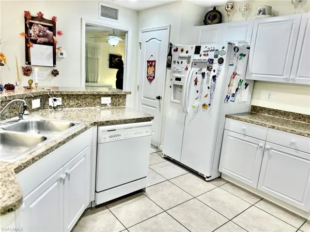Kitchen with white cabinets, white appliances, light tile patterned floors, and a ceiling fan