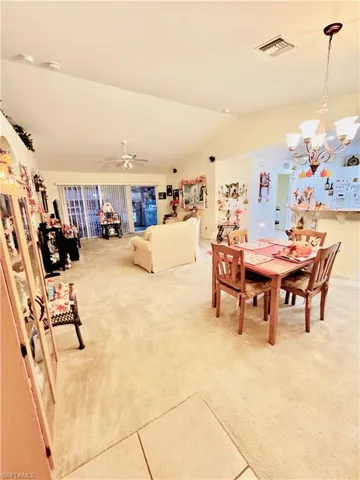 Dining room with light carpet, vaulted ceiling, light tile patterned flooring, and a chandelier