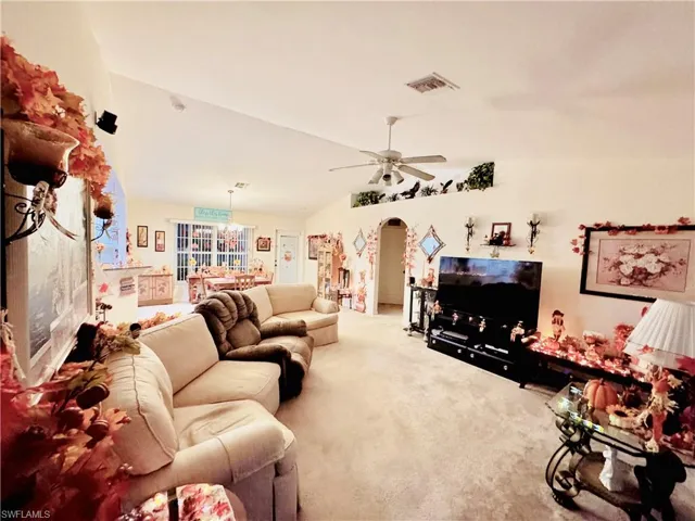 Living room featuring lofted ceiling, arched walkways, carpet, a chandelier, and a ceiling fan