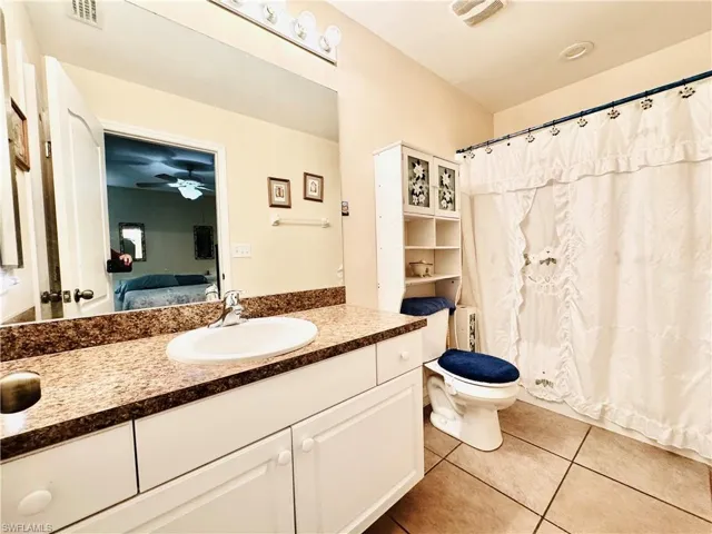 Full bath with vanity, connected bathroom, light tile patterned flooring, a ceiling fan, and curtained shower