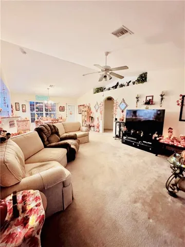 Carpeted living area with lofted ceiling, arched walkways, a ceiling fan, and a chandelier