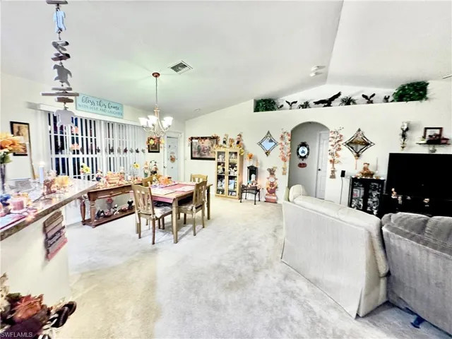Dining area featuring light colored carpet, vaulted ceiling, arched walkways, and a chandelier