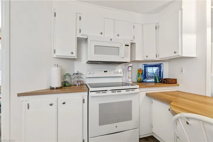 Kitchen with white appliances, white cabinets, and butcher block countertops