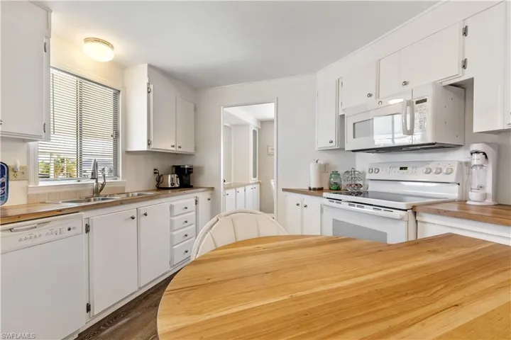 Kitchen with white appliances, wooden counters, and white cabinetry