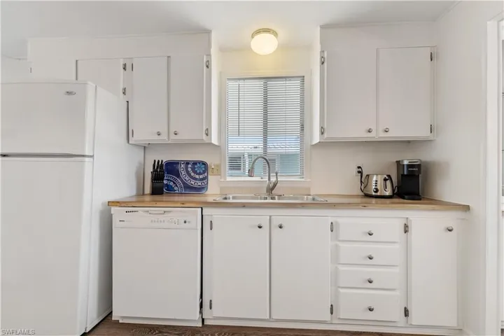 Kitchen featuring white appliances, white cabinetry, and wooden counters