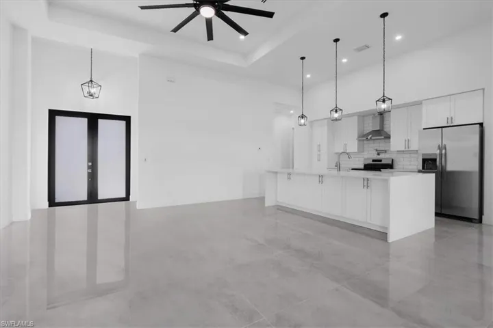 Kitchen with wall chimney range hood, decorative light fixtures, stainless steel appliances, white cabinets, and a large island