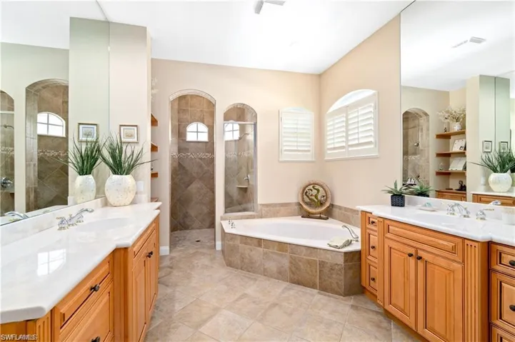Full bathroom with walk in shower, two vanities, and a garden tub