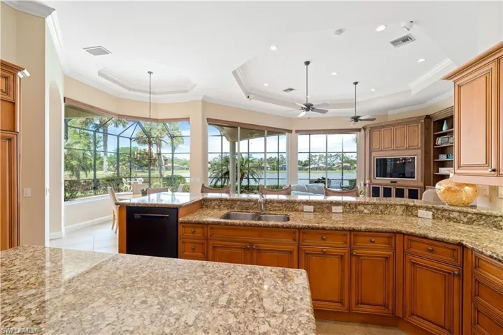 Kitchen featuring wood finish cabinets, plenty of natural light, light stone counters, black dishwasher, and ornamental molding