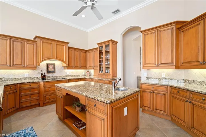 Kitchen featuring glass fronted cabinets, an island with sink, open shelves, wood finish cabinetry, and light tile patterned floors