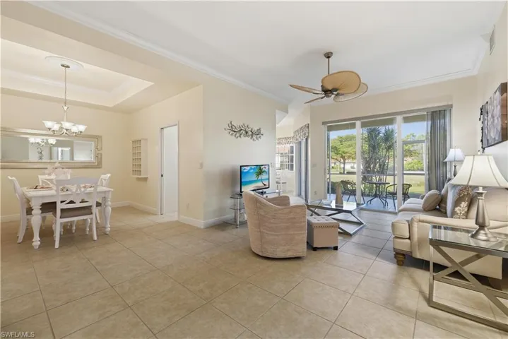 Living room with crown molding, light tile patterned floors, a raised ceiling, a chandelier, and a ceiling fan
