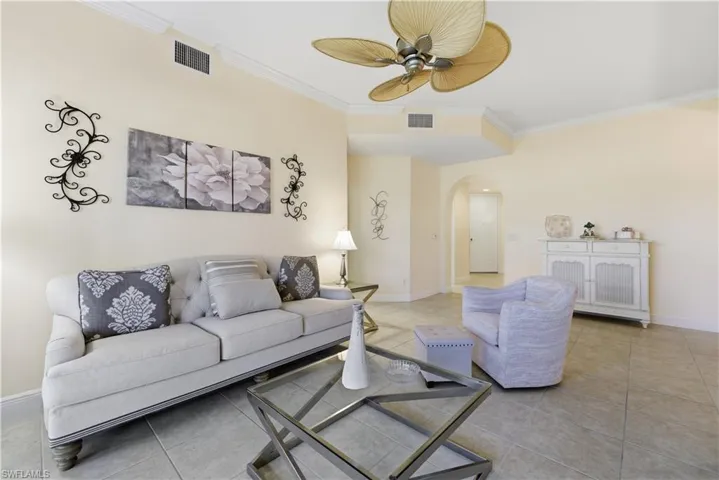 Living area with arched walkways, crown molding, light tile patterned flooring, and a ceiling fan
