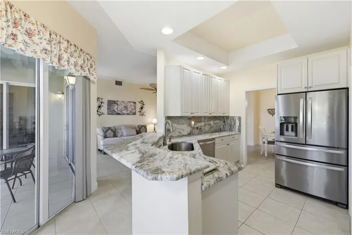 Kitchen with appliances with stainless steel finishes, light stone countertops, backsplash, light tile patterned flooring, and a raised ceiling