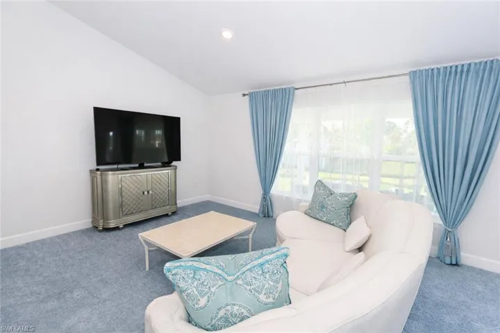 The living area features a vaulted ceiling, light blue carpeting, and a large window with light blue drapery