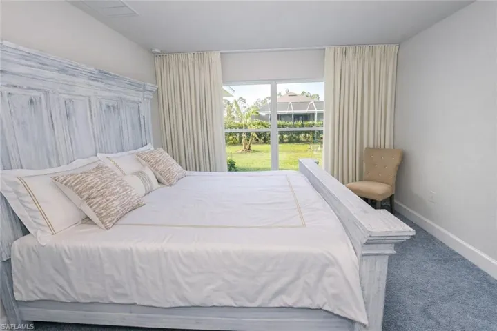 Bedroom featuring carpeted flooring and large windows with privacy curtains, overlooking a landscaped yard