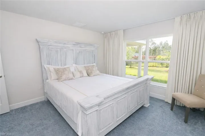The property features light blue carpeting, white walls, and a large window providing views of the outdoor landscape