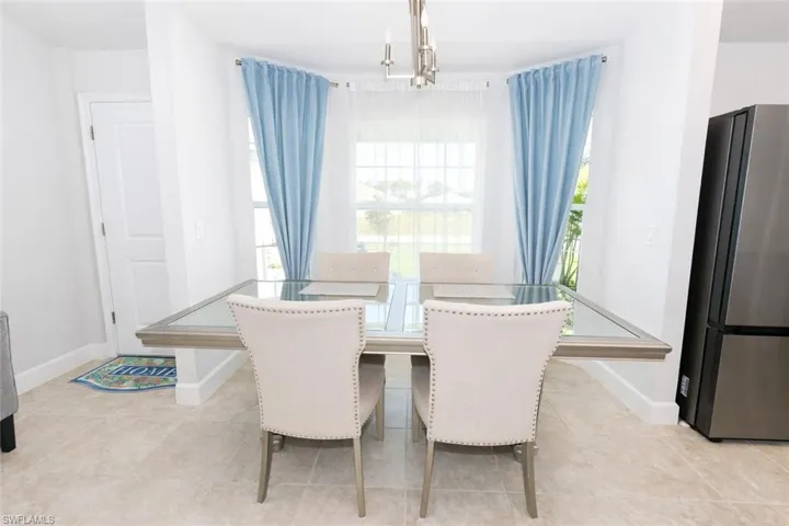 The dining area features light-colored tile flooring, a window with light blue drapery, and a modern light fixture