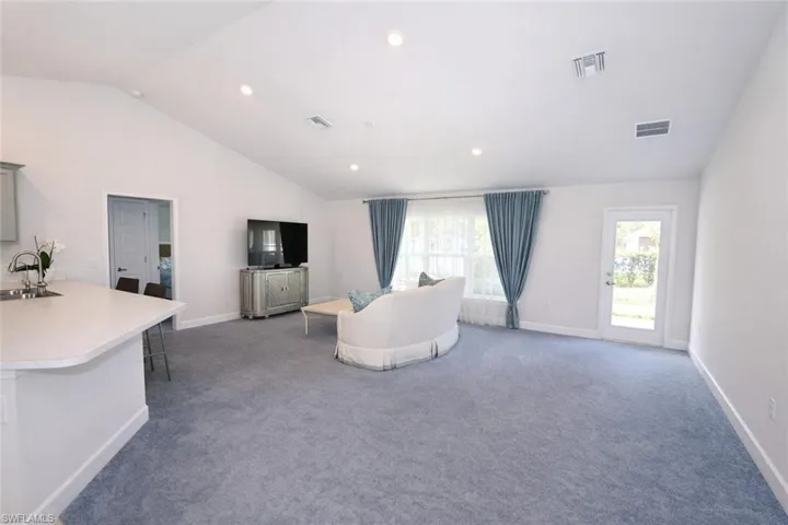 The living area features a vaulted ceiling with recessed lighting, light blue carpeting, and a glass-paneled door opening to the exterior